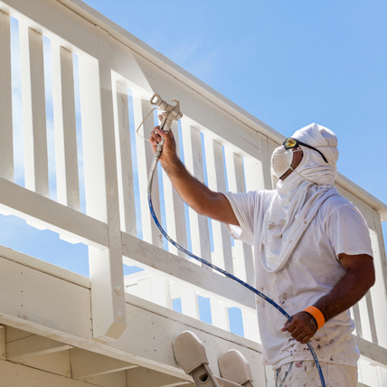 A person on a ladder spray painting a patio. 