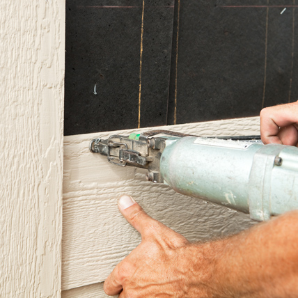 Hands using a nail gun to secure on siding. 